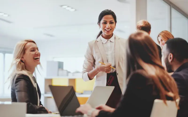 Three women and a man at a conference table smiling and talking
