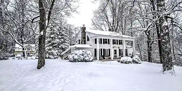 Large white house in the woods on a snowy day.