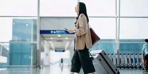 A woman walks through an airport with her passport and roller bag.