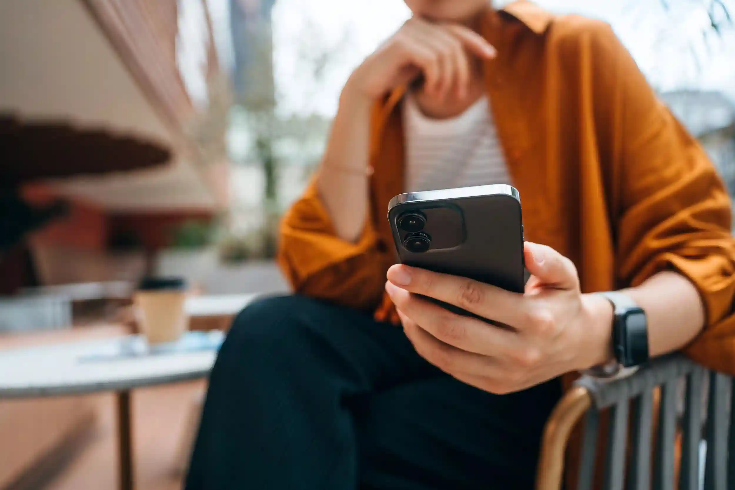 Woman holding phone sitting outside a coffee shop