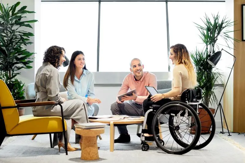 Three people sitting in chairs and one person sitting in a wheelchair talking
