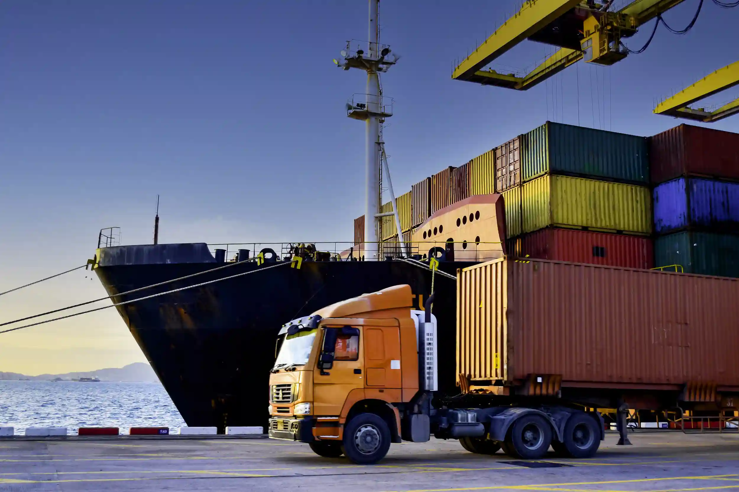 A truck driving past a cargo ship loaded with containers.