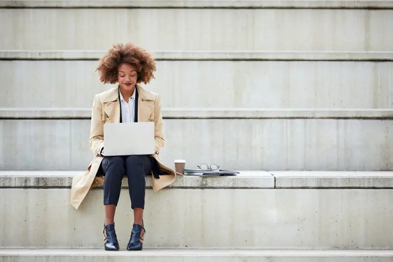 A black woman sitting and working with a laptop on her lap